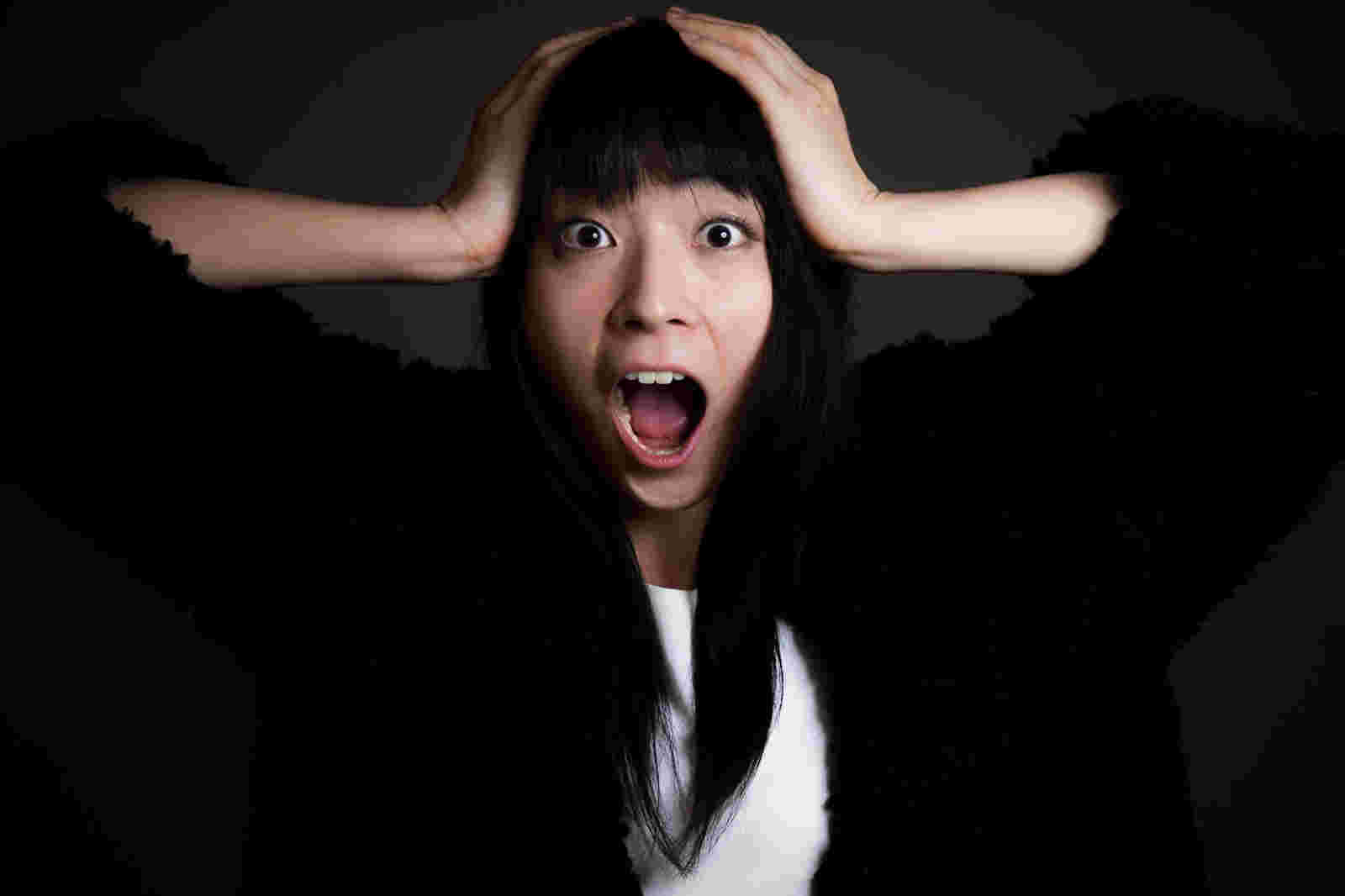 頭の横に両手をおいて驚いている女性