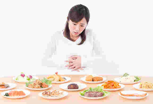 沢山の食事とお腹を押さえる女性