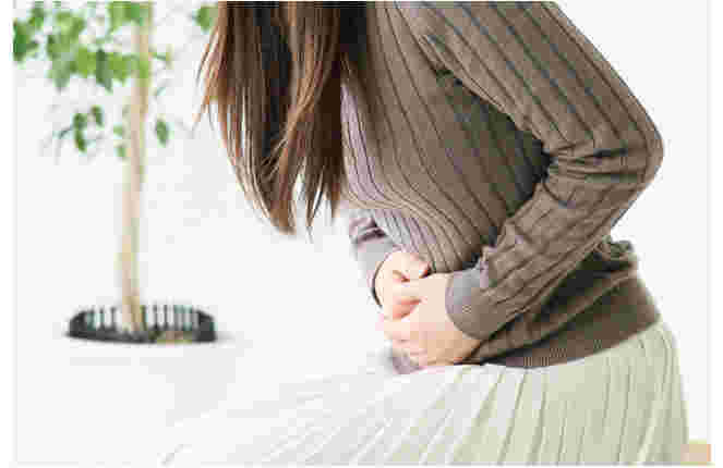 腹部を押さえて前かがみになる女性