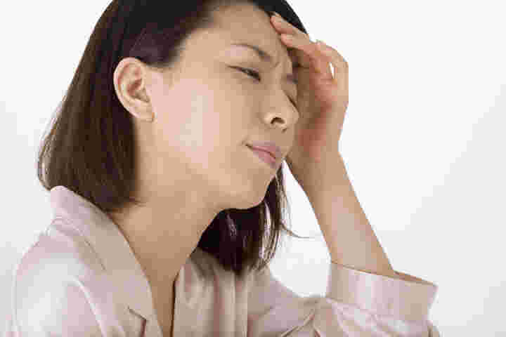 額を押さえて顔をしかめる女性