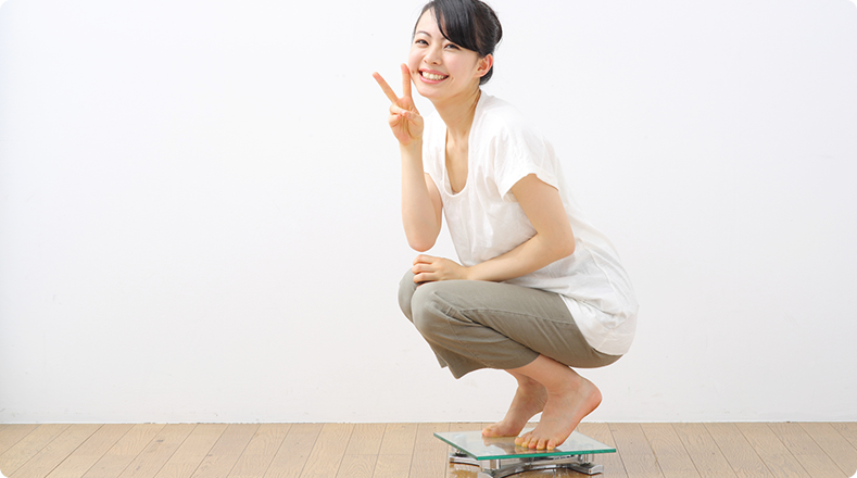 体重計に乗ってピースサインをする女性
