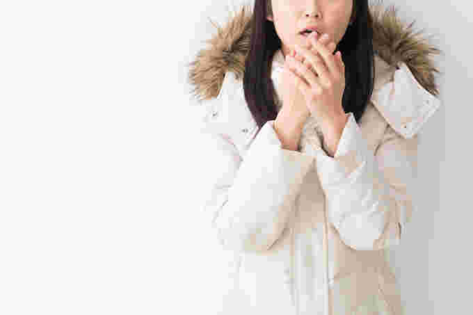コートを着て寒そうに息で手を温める女性