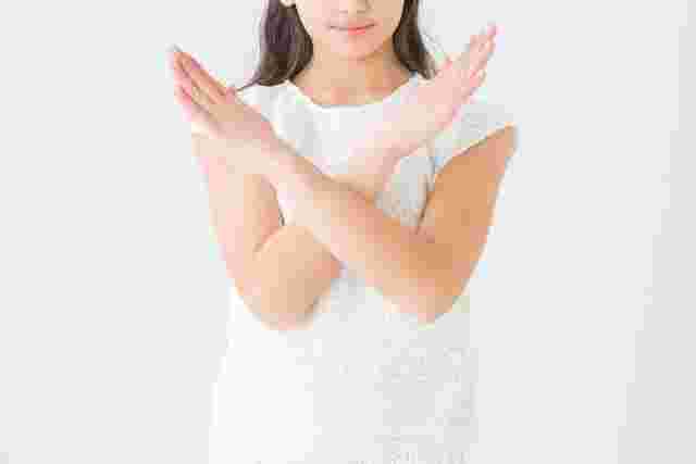 手でバツを作る白い服を着た女性