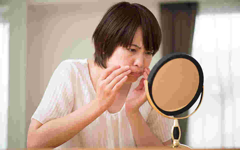 鏡の前でほうれい線を気にしている女性