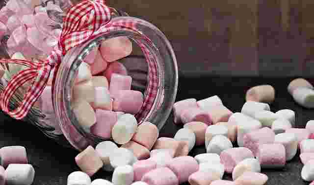 薄いピンク、オレンジ、白のマシュマロが瓶からこぼれ落ちている写真