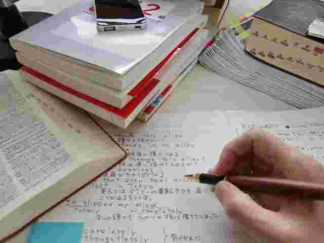 英語の勉強をしているところ。シャーペンを盛った手や広げられたノートや辞書などが写されている