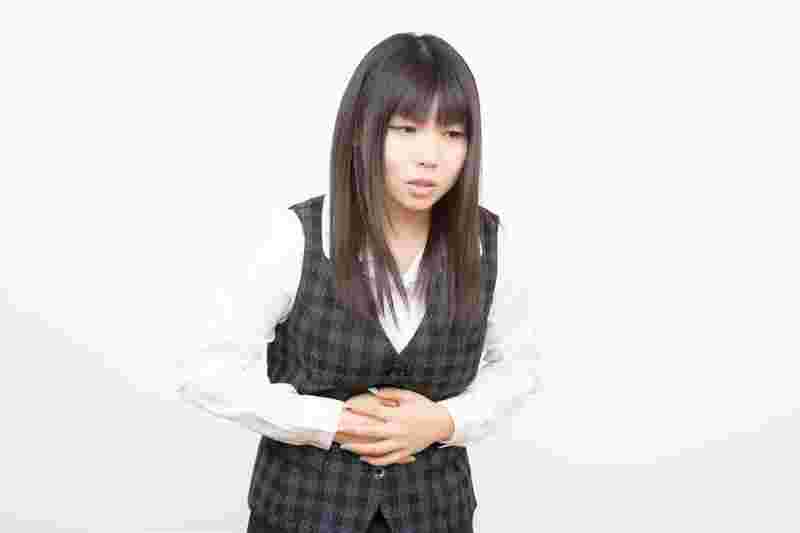 両手でお腹をおさえて痛そうな女性
