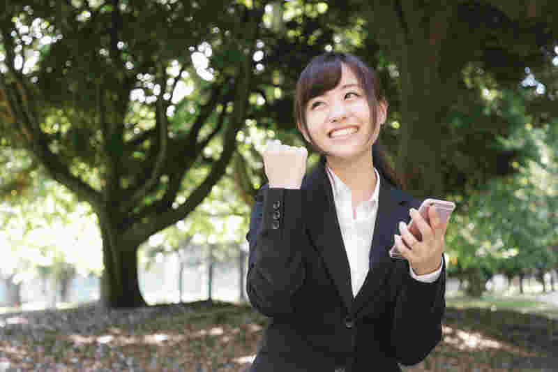 スマホを持ってガッツポーズをしているスーツ姿の女性