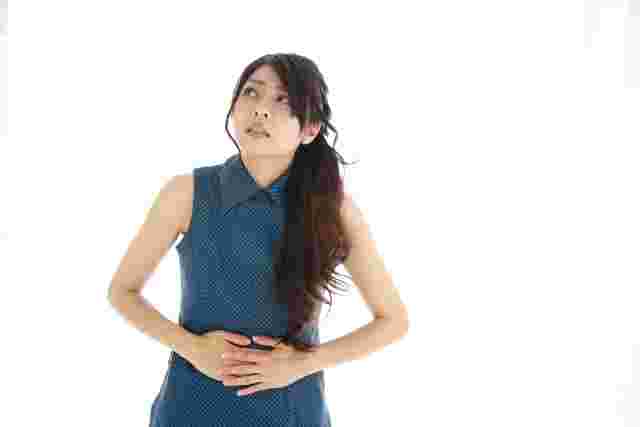 お腹を両手で押さえてしかめっ面の女性