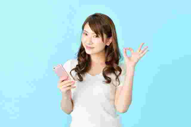 スマホを持ってオッケーサインを出す女性