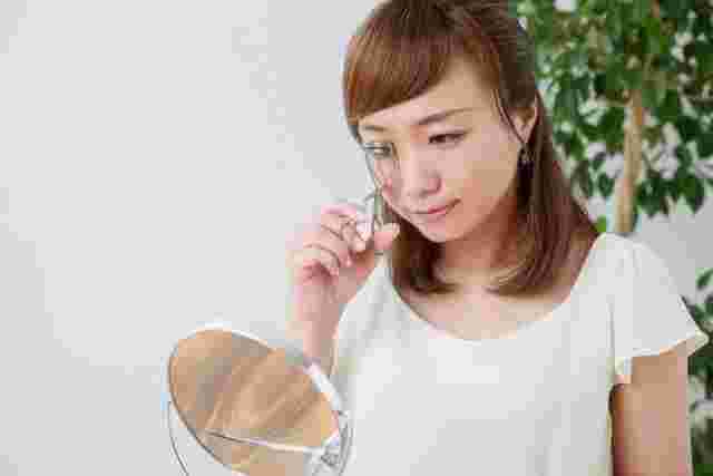 鏡を見ながらビューラーを目元に当てる女性