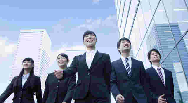 スーツを着た男女5人が街を歩いている様子。