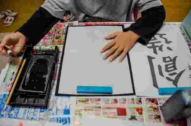 新聞紙を敷いてその上に墨汁と硯をおいて習字をしている子供