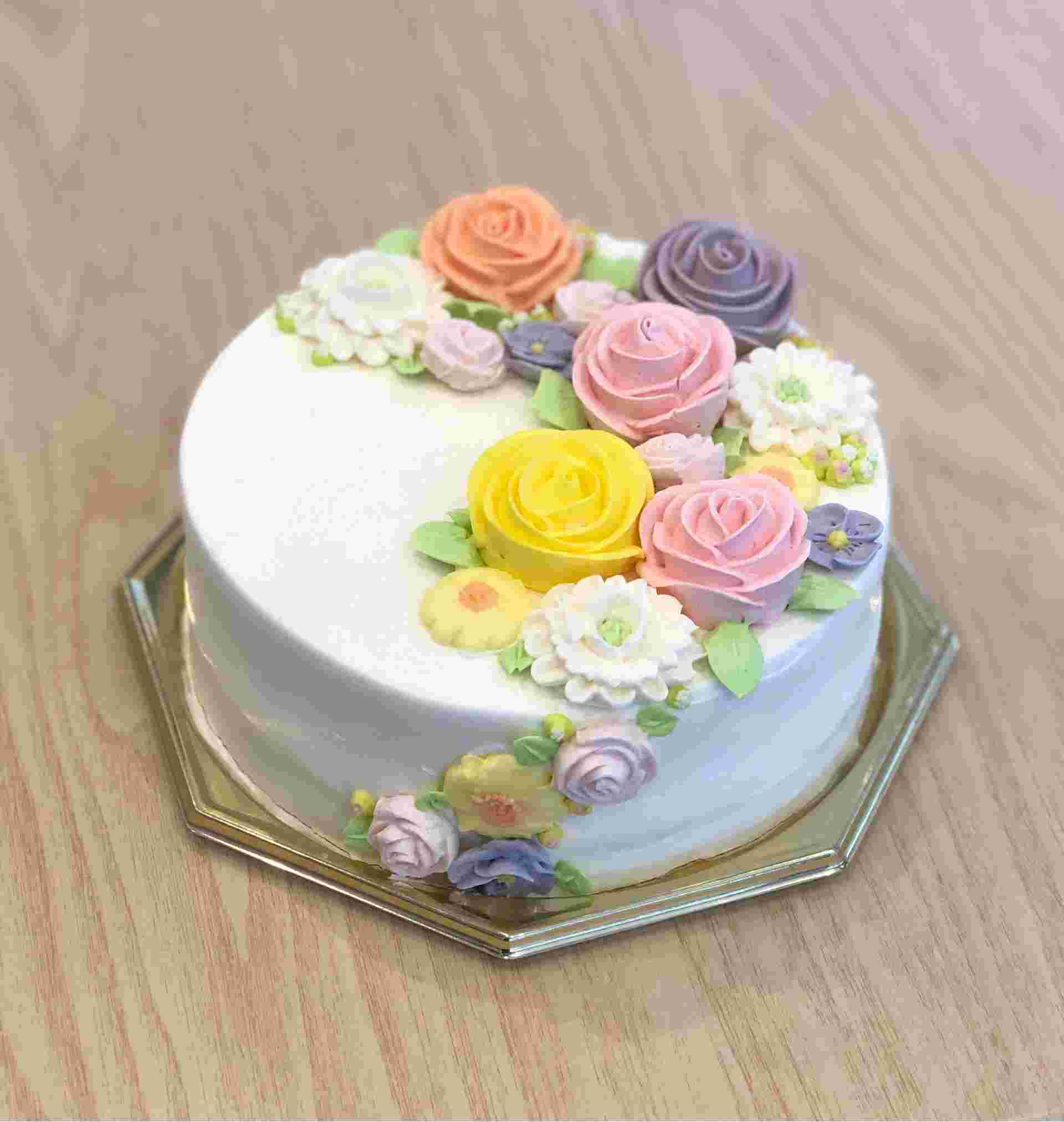華やかな花が装飾された真っ白なバタークリームケーキがテーブルの上に乗っている様子