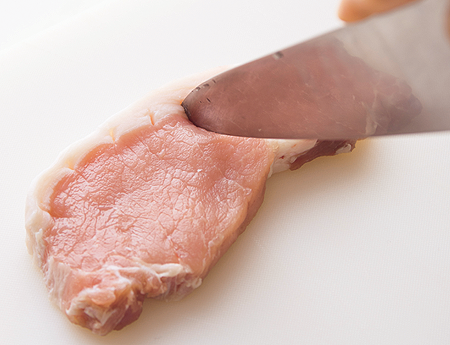 包丁で豚ロース肉の筋切り作業を行っている様子