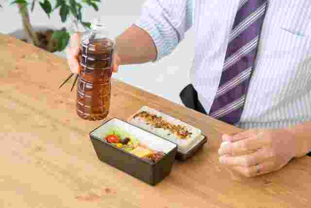 お弁当と一緒にペットボトルのお茶を飲む人