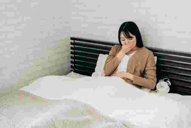 ベッドで口元をおさえる女性