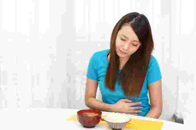 食卓で胃をおされる女性