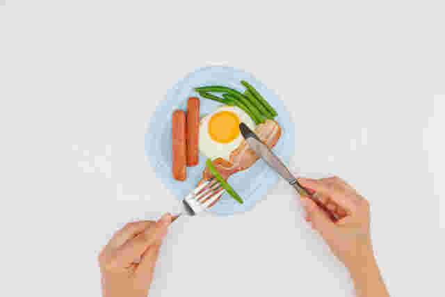 目玉焼きとウインナーと野菜をナイフとフォークで食べる様子