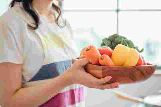 器に入った野菜を持つエプロン姿の女性