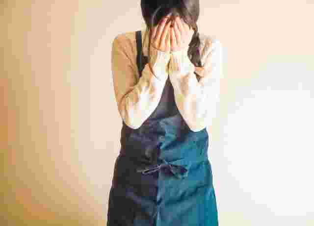 エプロンを付けた女性が顔をおさえている様子