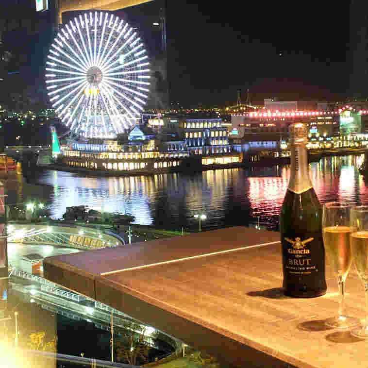 手前はテーブルの上にワインボトルとグラス、奥に夜景