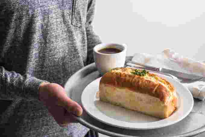 たっぷりと玉子が挟まれたパンとコーヒーをトレーで運ぶ女性