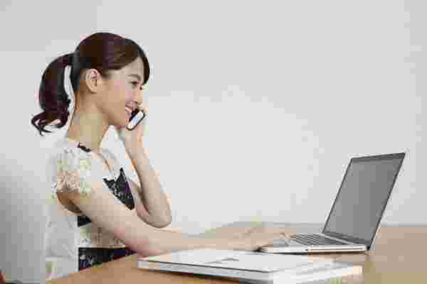 ホームページを見ながら電話をかける女性