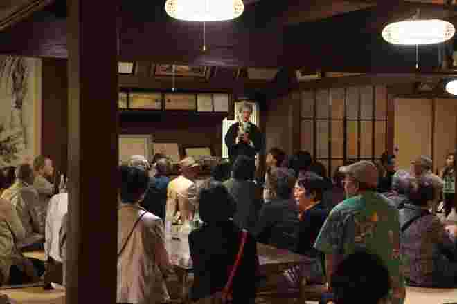 和室で日本酒の説明をしている女将と、多くの見学客