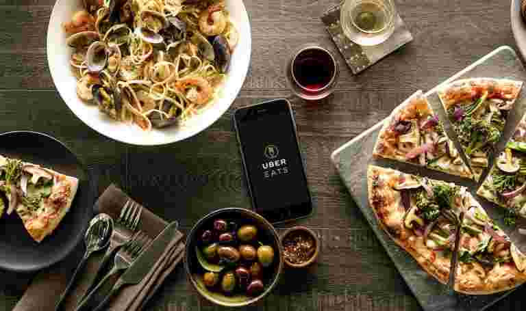 スマートフォンでウーバーイーツのアプリを表示　その周りに並ぶ料理