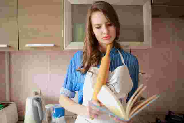綿棒を片手に持った女性が本を持ち悩まし気な表情を浮かべている