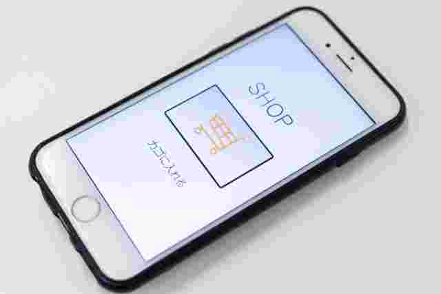 スマートフォンの画面に「SHOP」「カゴに入れる」と書かれており、カートの絵が描かれてます。
