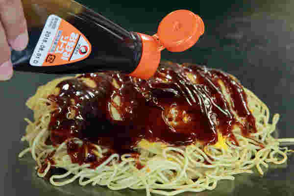 広島のお好み焼きにソースをかけているところ