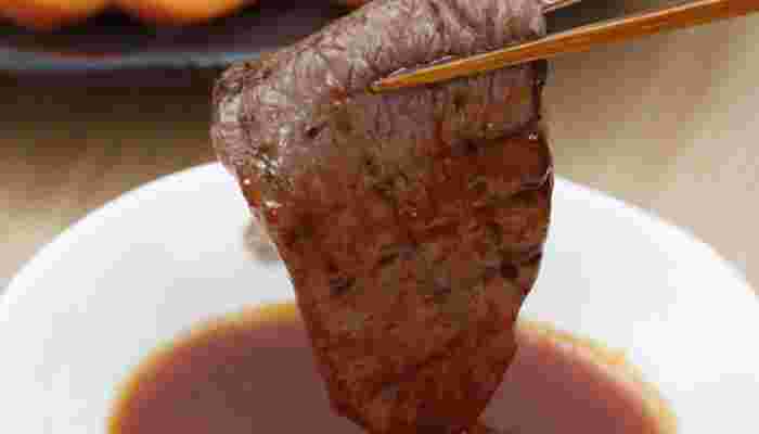 焼けたお肉をタレにつけている