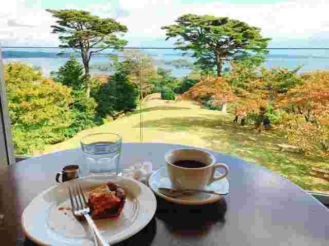 コーヒーとケーキが置いてあるテーブルと、松島の海が見える絶景の画像