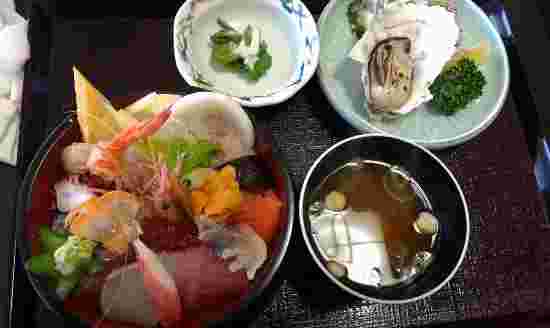 海老やウニ、マグロやカツオ、イクラやサーモンの乗った海鮮丼と焼き牡蠣などのお膳の画像