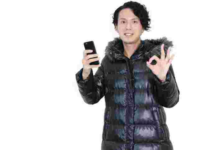 スマートフォン片手にOKサインをする男性