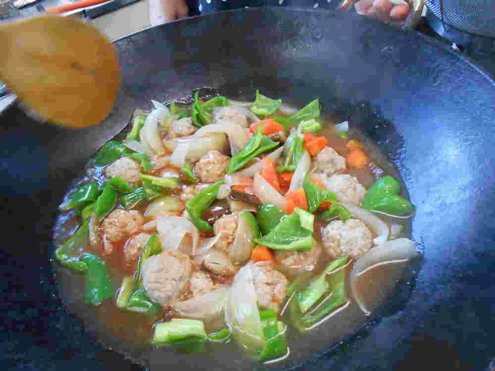 野菜をたっぷり鍋で炒め合わせている肉団子の酢豚風
