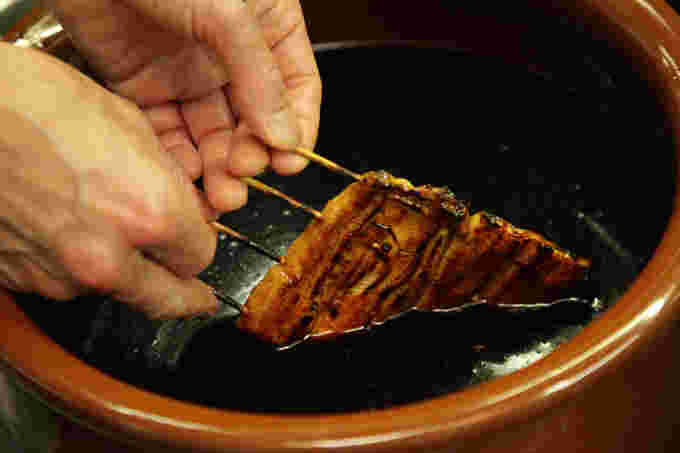 うなぎのタレが入った壺につける美味しそうな蒲焼き