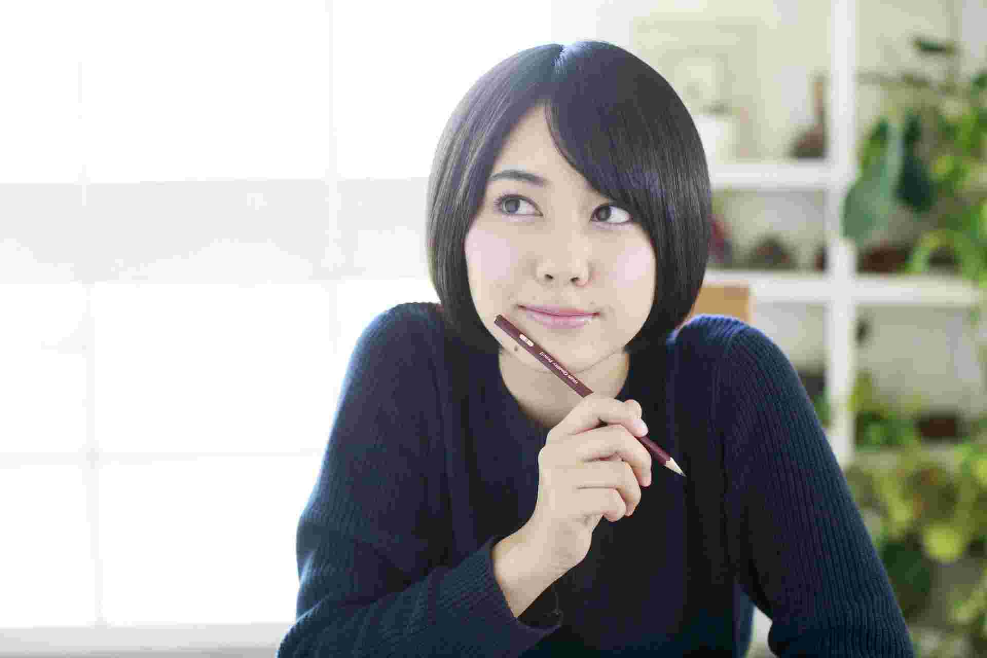 鉛筆を持って斜め上を見ながら考え込む女性