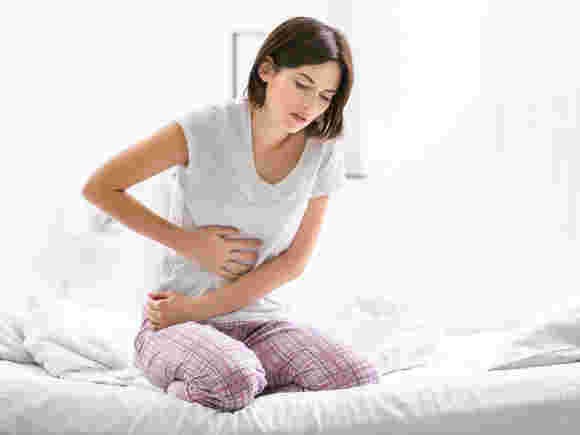 両手でお腹を押さえベッドの上で苦しそうにする女性