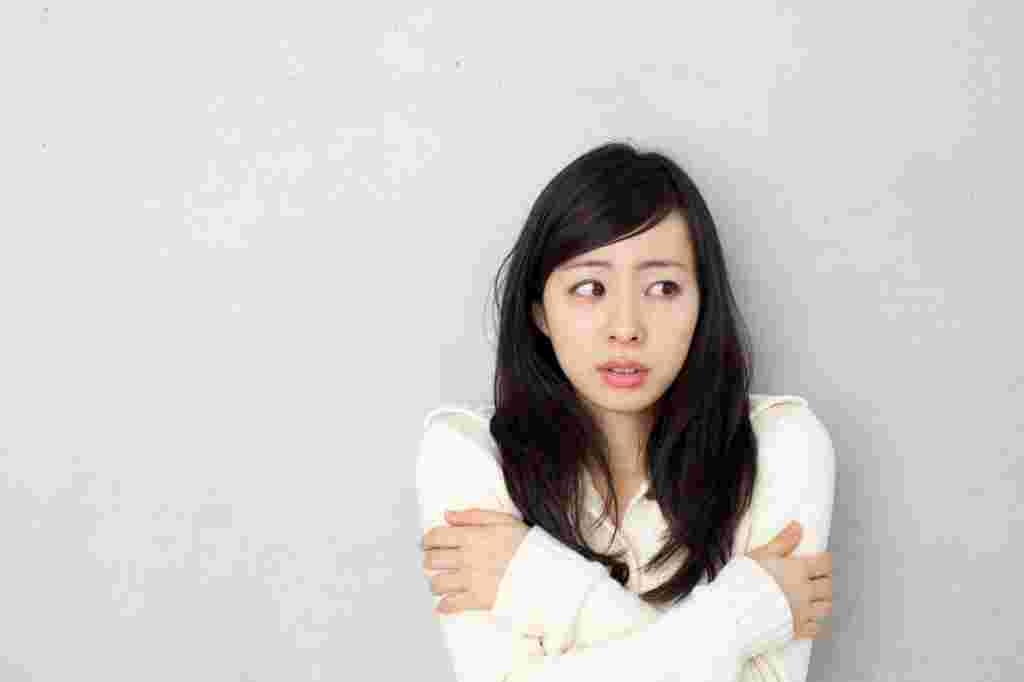 寒そうに両手で腕を抱えこむ女性
