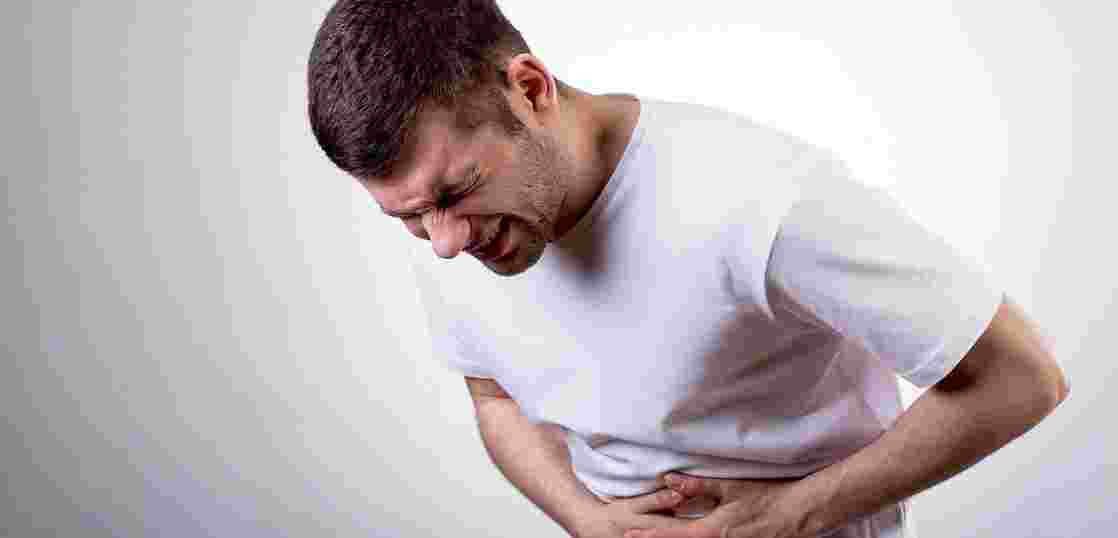 痛そうに両手でお腹を押さえて前かがみになる男性