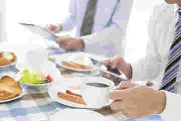 スマホとタブレットを片手に食事をしているビジネスマン