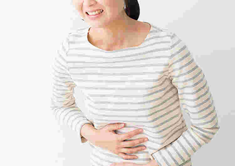 みぞおちを押さえて痛そうにしている女性