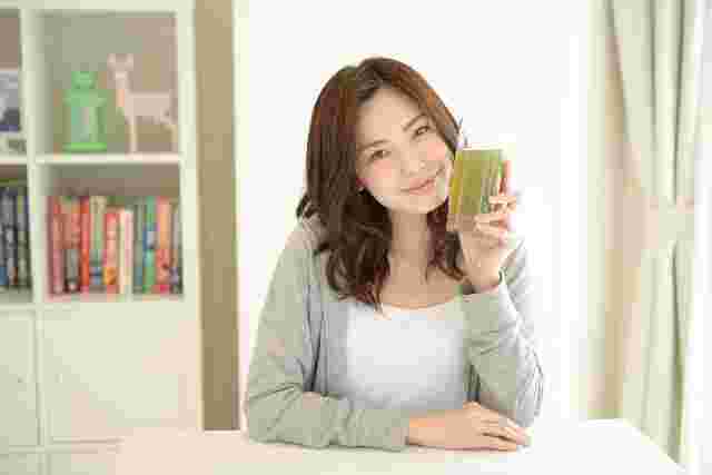 緑茶の入ったコップを頬に当てながら笑顔の女性