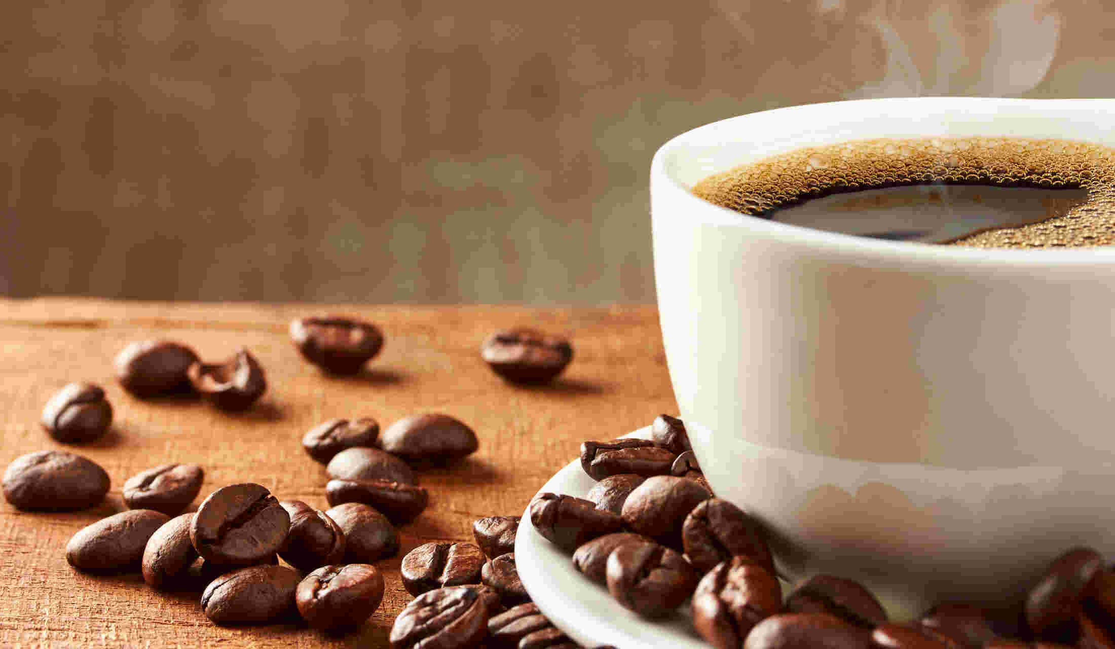 湯気立つコーヒーと周りに散らされた豆