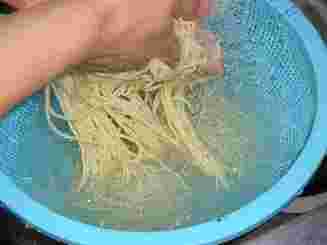 青いザルで麺をそうめんを洗っている。