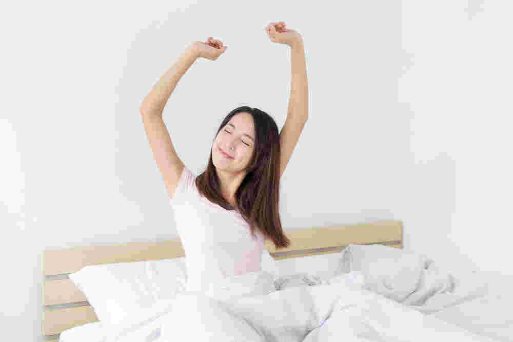 ベッドから起き上がって気持ちよさそうに伸びをする女性