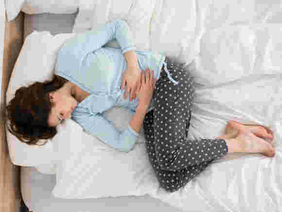 お腹を押さえながらベッドに横たわる女性「